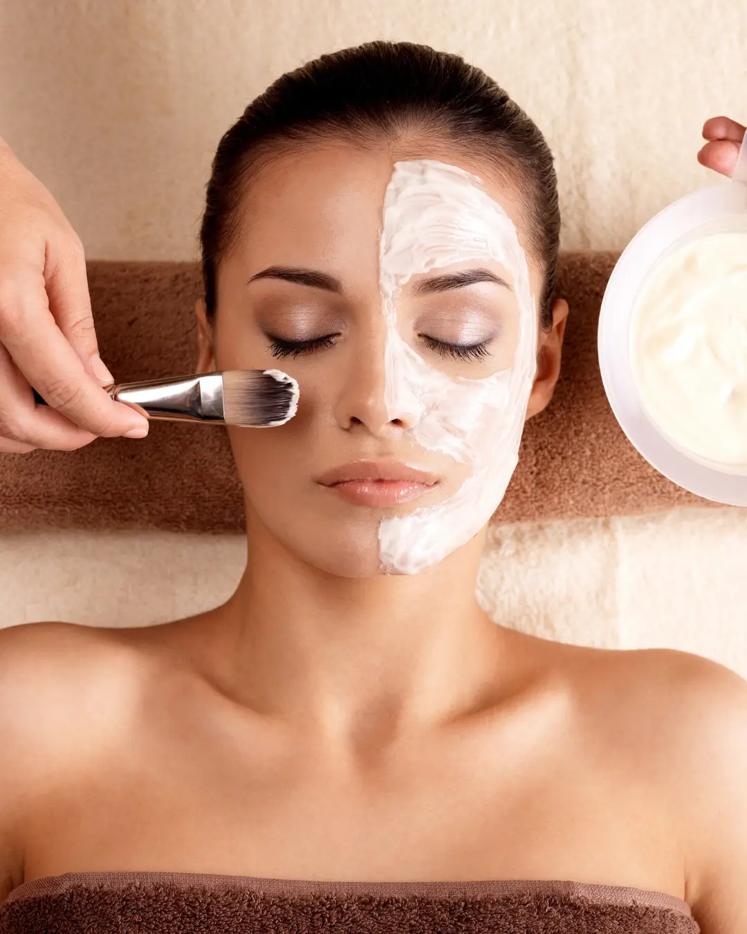 Woman receiving a facial treatment with a cream applied to half of her face, showcasing a relaxing spa environment, emphasizing customized skincare and clinical-grade results.