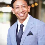 Dr Shiv Kumar Goel professional head shot- Smiling wearing grey color suit and a tie.