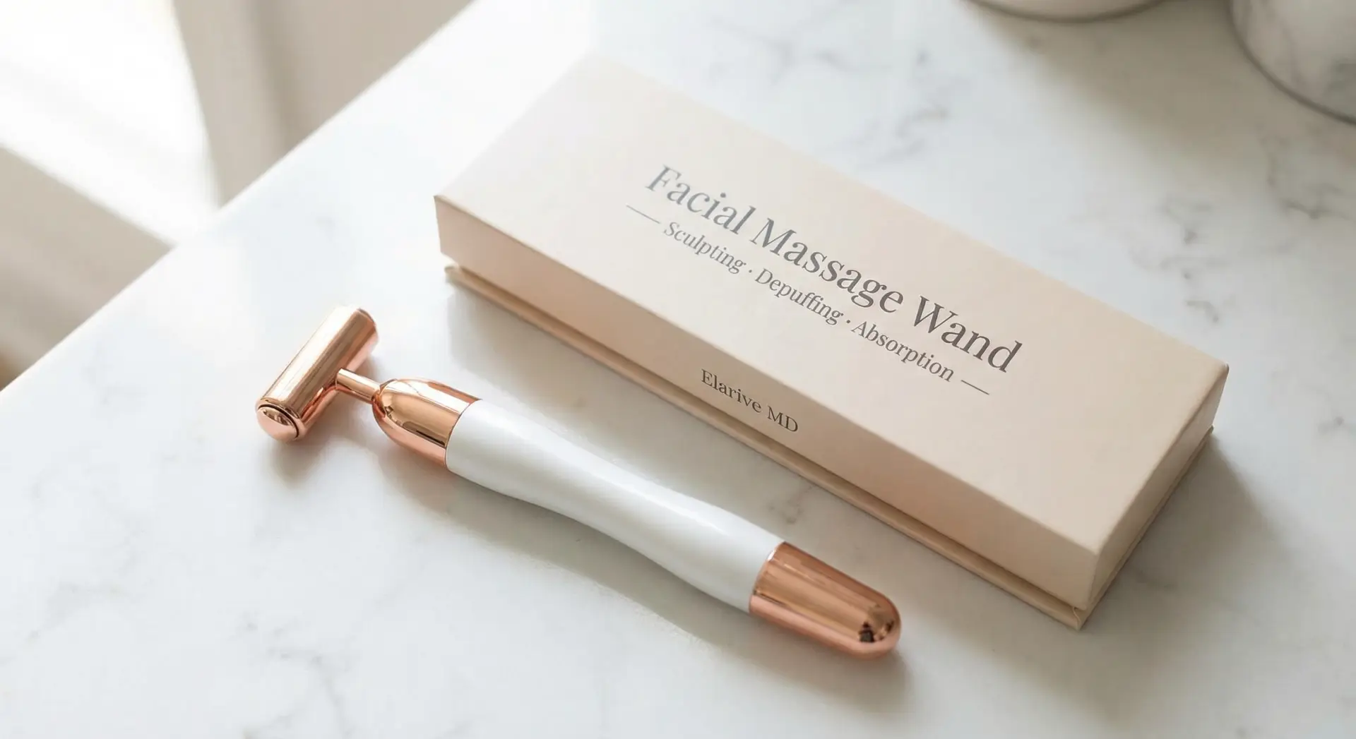 Facial massage wand with a white handle and rose gold accents, placed beside its packaging on a marble surface, emphasizing product absorption and depuffing benefits for skincare.