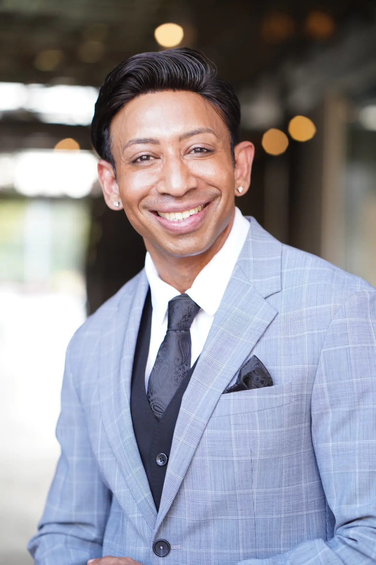 Smiling man in a gray suit with a black tie and pocket square, promoting men's health and wellness products at Prime Vitality Total Wellness and Medical Spa.