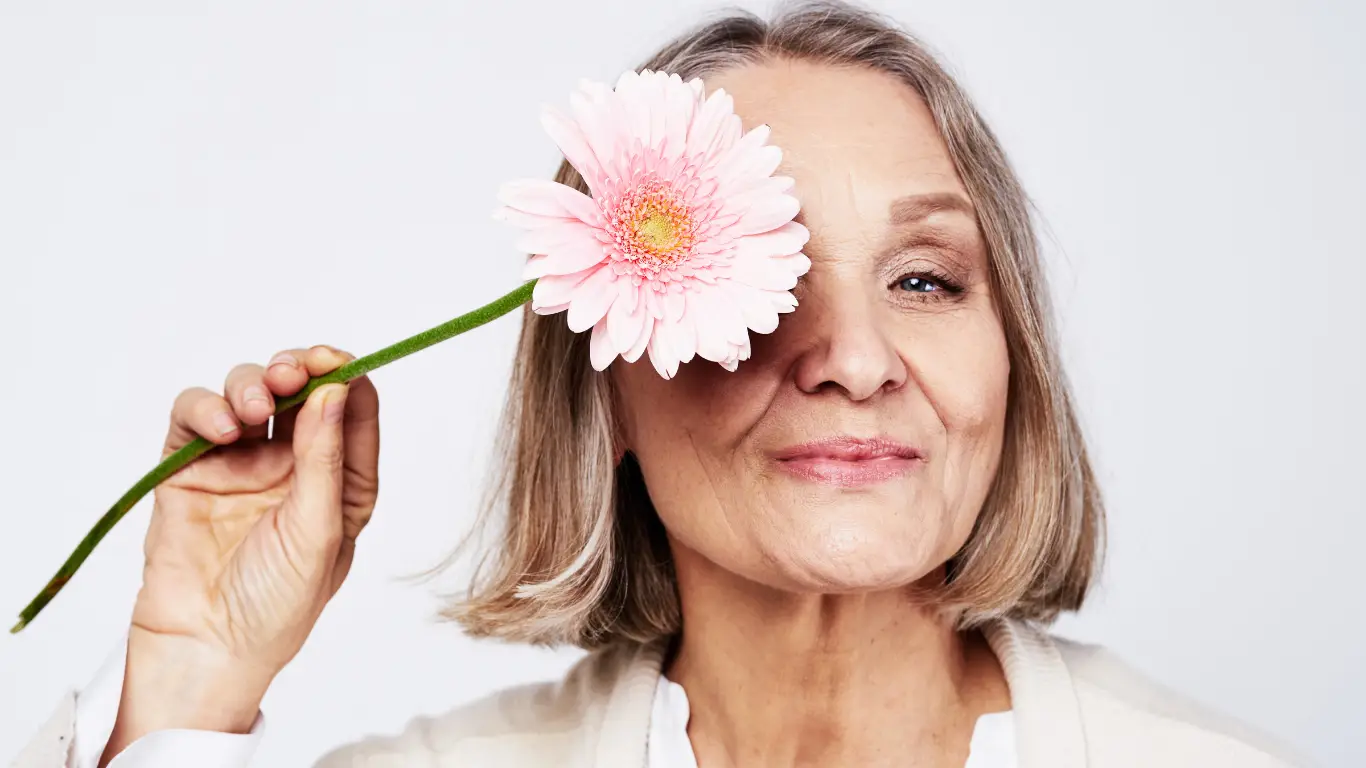 Smiling older woman holding a gerbera daisy, representing healthy ageing and longevity care at Prime Vitality Care in San Antonio.